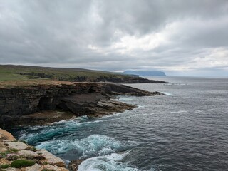Rocky coastline with waves crashing against cliffs in Orkney, Scotland.