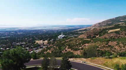 Drone flying above green hills landscape, to reveal bountiful Utah Temple with a nearby road