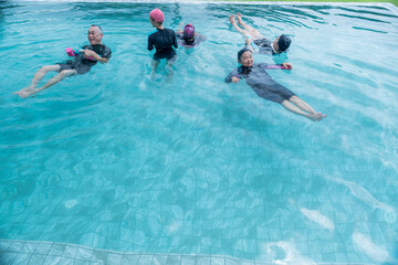 senior aquatic class practicing water relaxation and float techniques. Participants float with support, guided by an instructor in a serene pool, promoting wellness and calmness through water therapy.