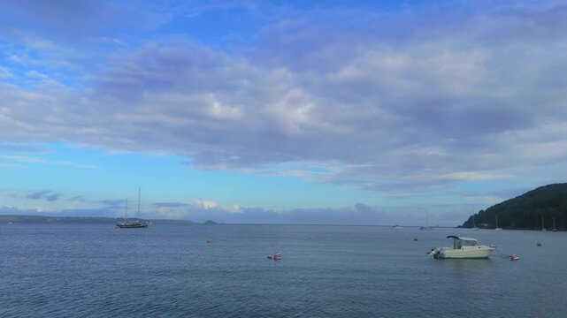 Drone flying over the sea towards and past a classic antique yacht sat at anchor, at Cawsand Beach