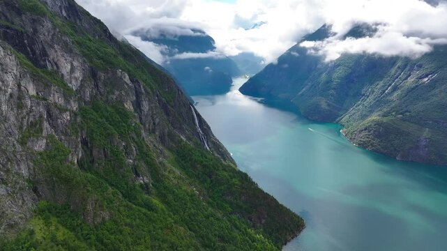mountains landscape and fog surrounding a blue tranquil body of water in the Geiranger Fjord