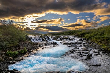 Bruarfoss Waterfall landscape with clear blue water at sunset.