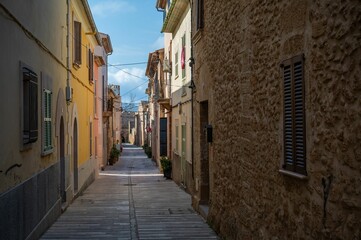 Obraz premium Narrow alleyway in a village with colorful buildings and a clear blue sky in Alcudia, Mallorca