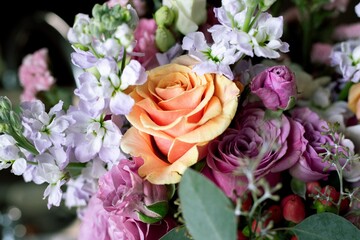 Close-up of a vibrant bouquet with an orange rose and purple flowers.
