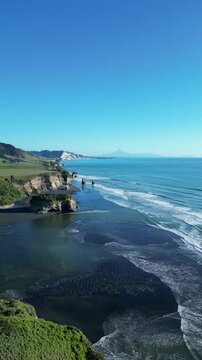 Drone pullback of the blue sea with green rocky shore at the Three Sisters Lookout, on a sunny day