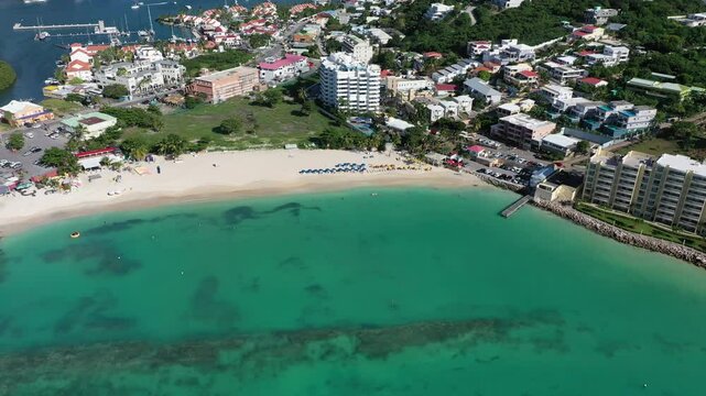 Drone over the ocean and beach with coastal buildings, and mountain in the background in Simpson Bay