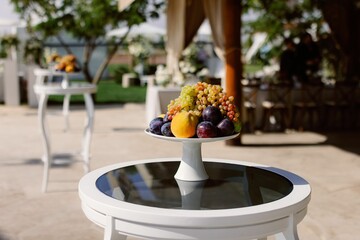 Elegant fruit arrangement on a white table in an outdoor setting, with grapes, plums, and peach