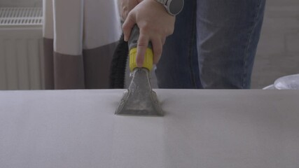 Closeup of man's hands holding nozzle of vacuum cleaner and cleaning a Mattress indoors