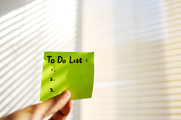 Close up of Hand Holding Sticky Note With To Do List on Wall	
