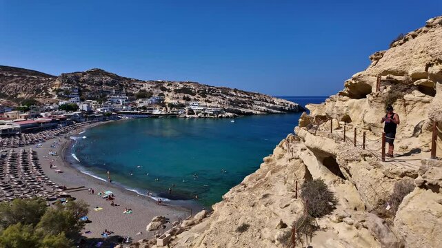 Climber explores ancient Matala Caves overlooking turquoise bay on a sunny day in Greece