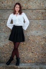 Young woman in a white top and black skirt posing against a stone wall