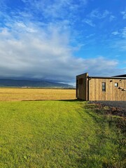Wooden cabin on green field under blue sky in Iceland.