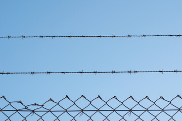 view of a wire fence with barbed wire on top of it on a blue sky day