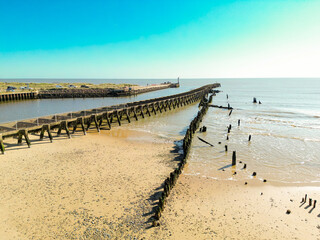 Fototapeta premium Decaying wooden groyne seen extending out to sea from a golden beach on the Suffolk coastline. A channel is on the left leading to the River Blythe.