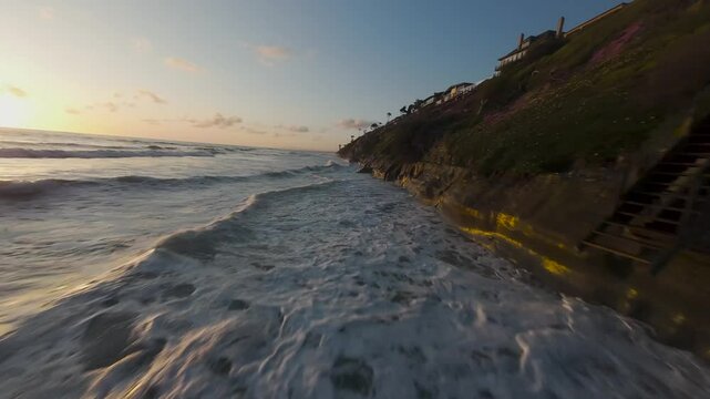 ocean waves breaking onto the cliff on Moonlight State Beach at sunset in Encinitas, California