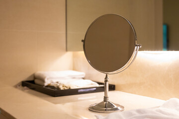 A bathroom mirror sits on a counter next to a tray of towels