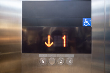 A digital screen on an elevator shows a downward arrow and the numbers 1, 2, 3 for handicap person.