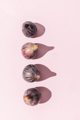 Four purple figs casting strong shadows on light pink background