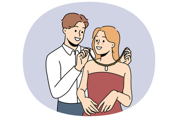 Loving man puts necklace around girlfriend neck to help get ready for party. Rich boyfriend courts girl and gives precious necklace as sign of seriousness of romantic relationship.