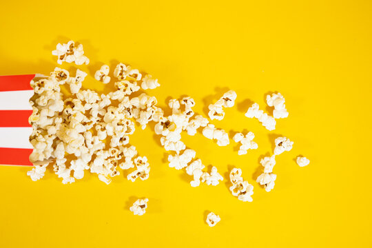 Top view of red carton bucket with white lying down. spreading popcorn on yellow background, concept of food and cinema entertainment