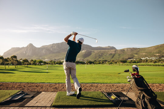 A male golfer elegantly swings his club on a picturesque mountain course at a golf resort