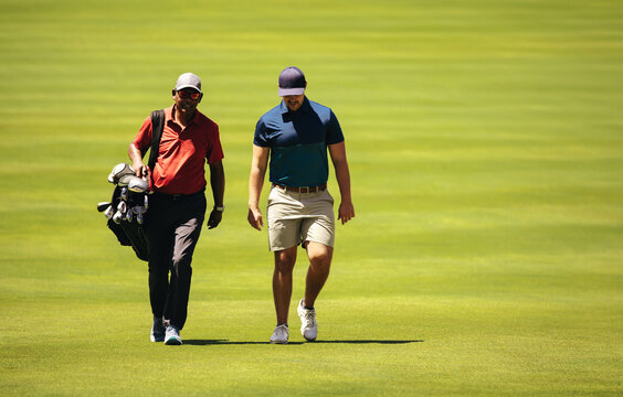 Caddy and golfer walking together on a sunny day, discussing strategy on the golf course during a competition