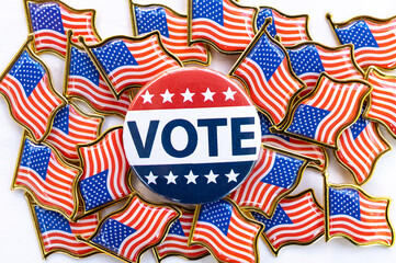 Vote button with American flags background.A close-up image of a prominent "VOTE" button surrounded by several small American flag pins. Button features patriotic colors, stars, emphasizing election
