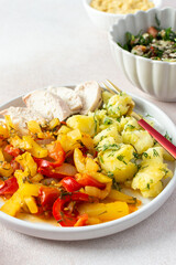 A balanced meal of boiled potatoes with baked vegetables and chicken breast, paired with a fresh tomato and cucumber salad topped with seeds