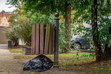 garbage in a black bag lying under the basket. people litter in the city park. © Adam