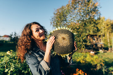 Smiling woman with curly hair holding a sunflower, radiating happiness and positivity. Woman celebrating the harvest festival, holding a sunflower on her rural farm with a smile