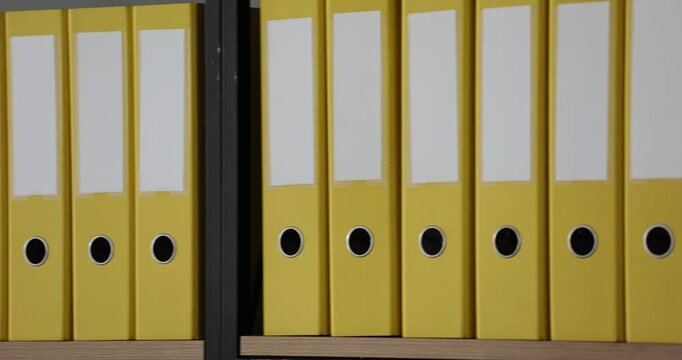Mockup with a white label on the spine of yellow folders with office documents standing on a wooden shelf in row. Storage of business documents