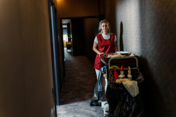 Obraz premium Cleaning lady with housekeeping trolley working in dim light hotel hallway.