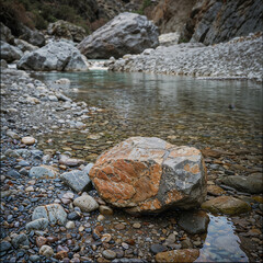 Fototapeta premium Rocky riverbed with a large boulder in a mountainous landscape
