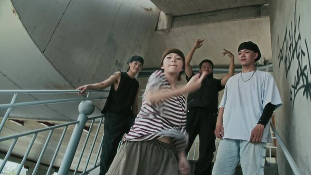 Low angle view of gen Z girl wearing streetstyle clothes showing dynamic moves on camera while dancing with friends on staircase