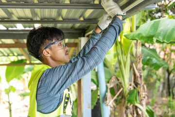 Male electrician wearing safety glasses and cloth gloves installs white plastic pipe to wiring...