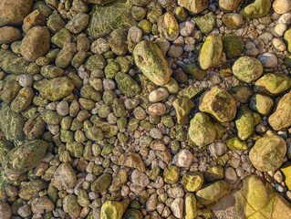 Closeup of sea ​​waves wash the pebbles on the shore. A colorful rocky riverbed at sunset with vibrant stones and clear water reflections. Macro pebbels