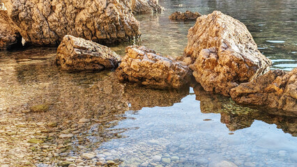 Clear waters reflect rugged rocks in a serene coastal setting during a sunny day by the shoreline, Majorca, Spain