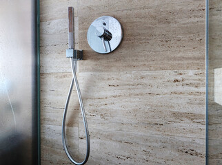Close up of modern shower fixture against a textured stone wall in travertine in a sleek bathroom ....