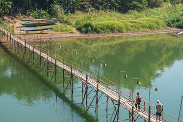 A beautiful green scenery where people is crossing the famous bamboo bridge in Luang Prabang, Laos and a reflection from the river 