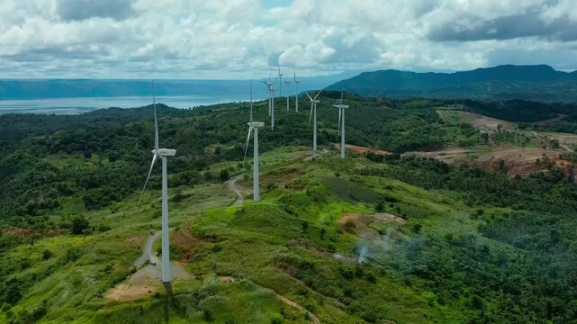 Empty road along mountaintop with wind turbines in Philippines in Pililla Rizal. Cloudy and stormy day on island producing energy of wind farm. Aerial wide shot.