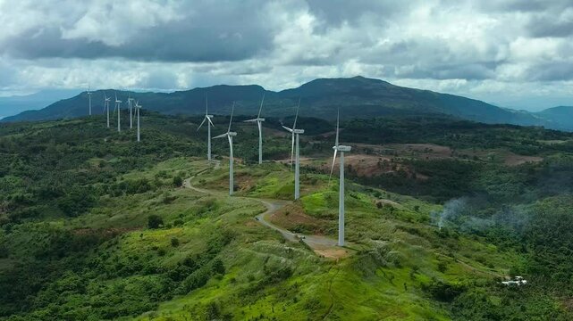 Aerial panorama view of burning fire between wind turbines on mountain in Philippines in Pililla Rizal. Rotating wind mills in green hills. Production of wind energy theme. Wide shot.