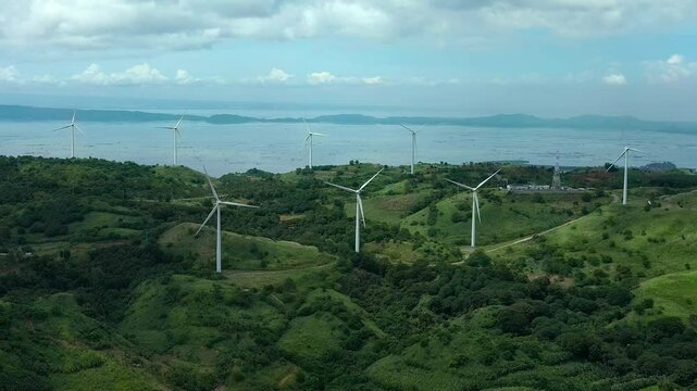 Aerial lateral wide shot of wind farm with wind turbines on coast of Philippines in Pililla Rizal. Cloudy stormy day with sea in background.