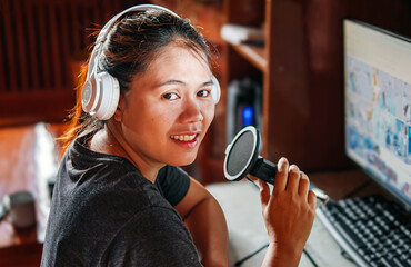 Smiling  and positive Asian female podcaster or radio host is wearing headphones, conducting her...