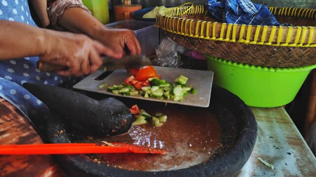 A female chef cuts tomatoes on a tray. Preparation for making lotek, Indonesian food containing vegetables and rice cakes drizzled with peanut sauce