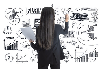 Businesswoman seen from the back drawing charts and graphs on whiteboard, holding documents. Black...
