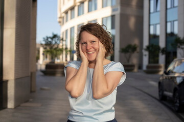 woman with curly short hair smiles and looks at the camera, holds both hands in cheerful amazement...