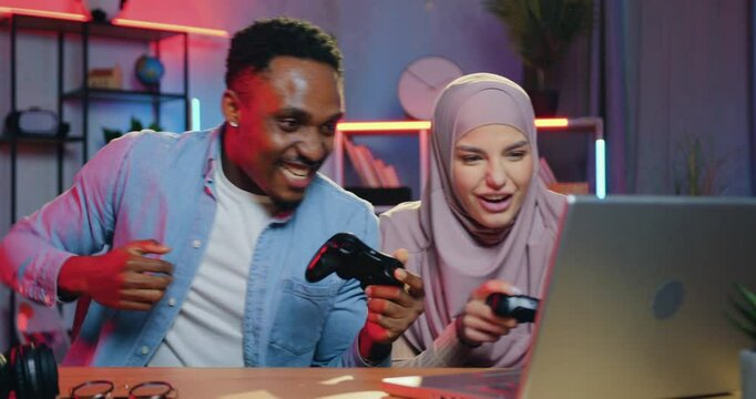Man celebrating victory in video game over his woman partner during competitions on computer in home office in the evening