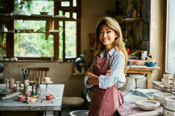 Pretty female artist smiling and posing at creative workshop with her artwork in the background.