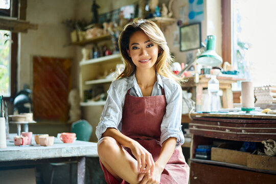 Pretty female artist smiling and posing at creative workshop with her artwork in the background.