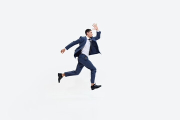 Man in suit runs energetically with determined expression, in mid-air as if striving towards something against white studio background. Concept of DEI, business, partnership, work, support and unity.